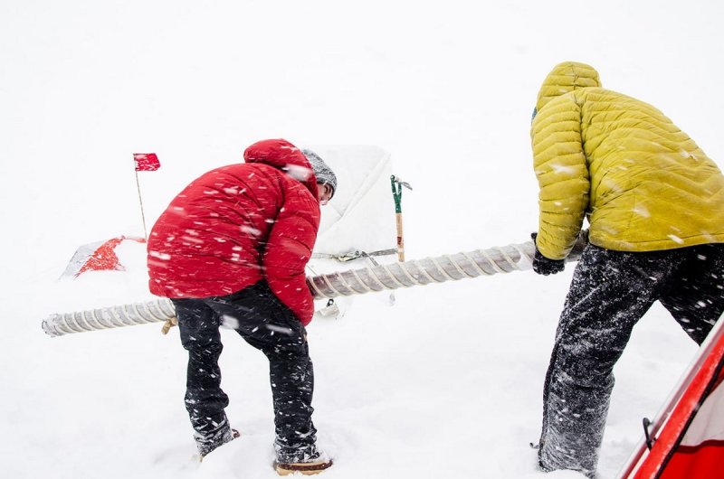 Matthew Osman (left) and Mike Waszkiewicz position an ice core during a storm in West Greenland. (c) Sarah Das, Woods Hole Oceanographic Institution