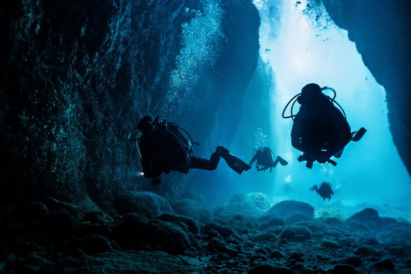 Diver swimming toward blue open water inside the Inland Sea tunnel during Gozo diving